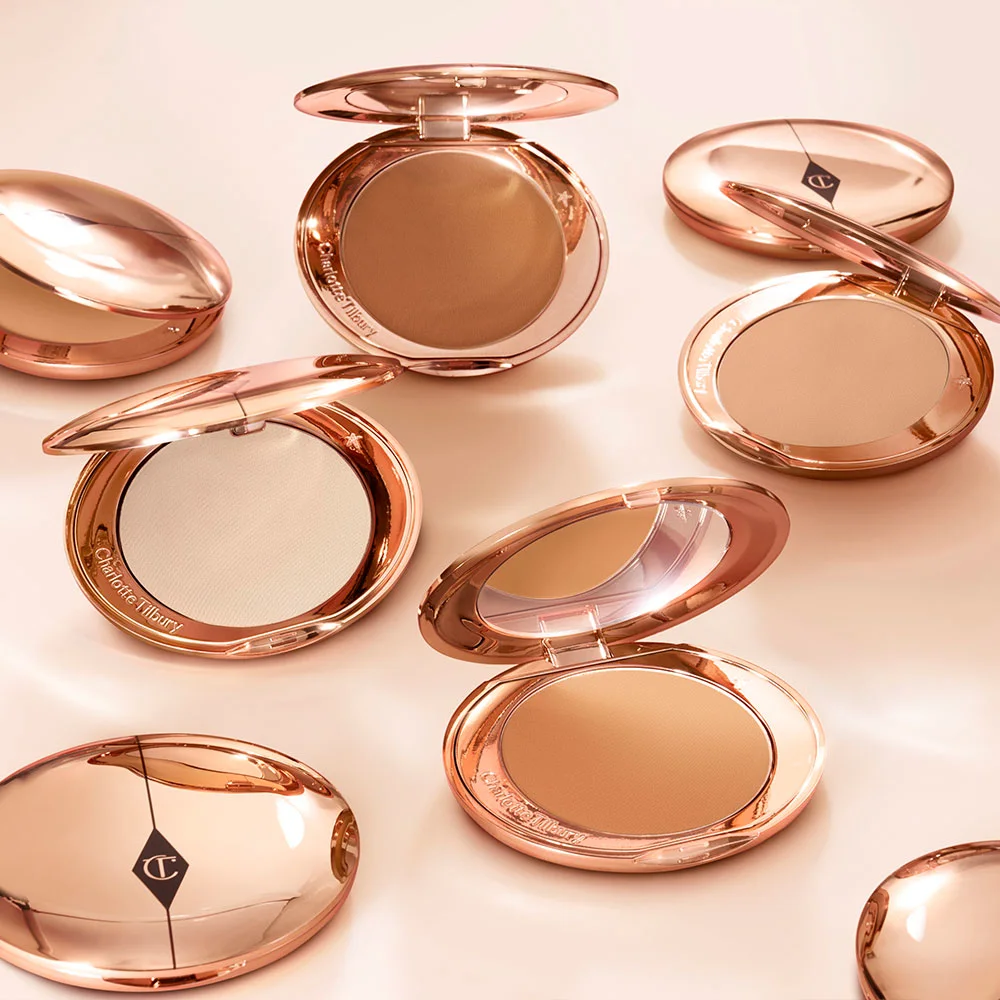 A collection of pressed powder compacts for light, medium-light, fair, and deep tones, in gold-coloured packaging with mirrored lids.